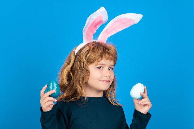 Niño en orejas de conejo mantenga huevos de Pascua aislado sobre fondo azul.