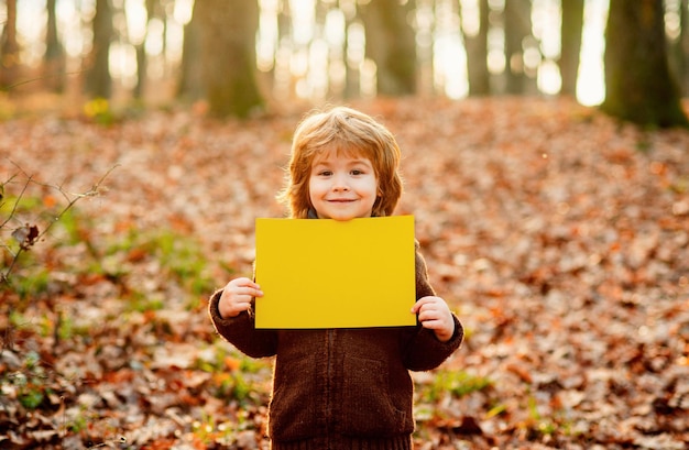 Niño de otoño sostiene una hoja en blanco para publicidad y venta de espacios de texto niño sosteniendo un tablero publicitario