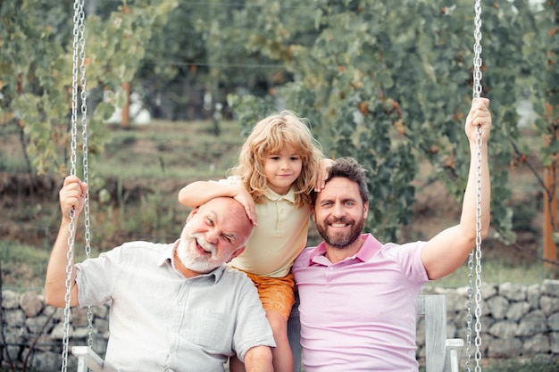 Niño con padre y abuelo columpiándose juntos en el parque al aire libre tres generaciones diferentes a...