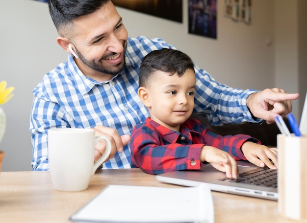 Foto niño con padre en casa usando computadora