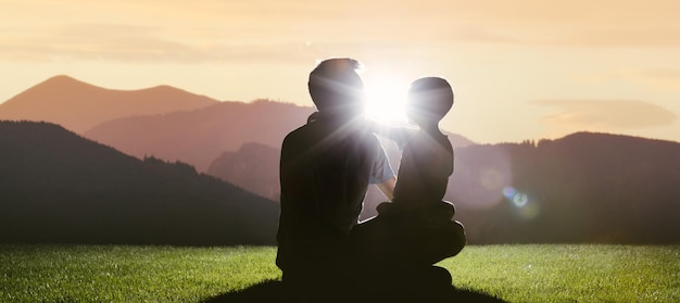 Foto el niño y el padre se sientan en la montaña y se encuentran con el amanecer del sol.