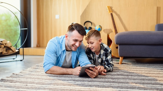 Foto niño con padre tirado en el suelo con tablet pc en apartamento moderno