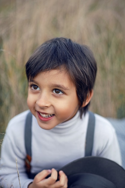 Foto niño en pantalones a cuadros, sombrero, tirantes y bufanda se encuentra en un campo