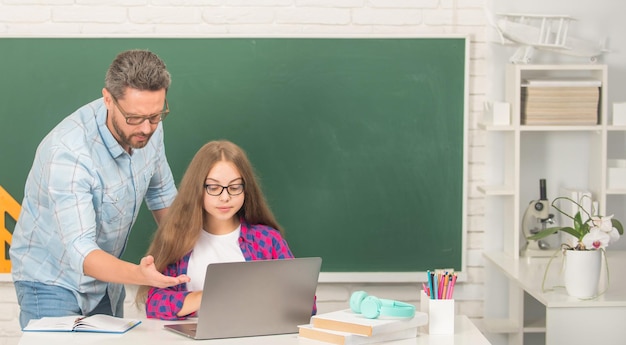 Niño y papá curiosos sentados en el aula con la computadora en la pizarra de regreso a la escuela