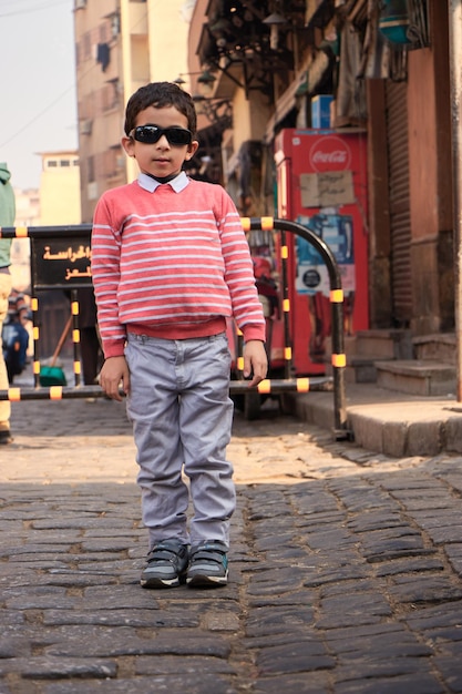 Un niño parado en una calle frente a una máquina expendedora de coca cola.