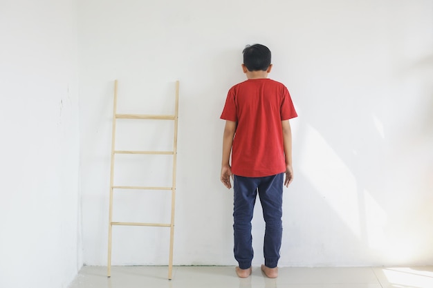 Niño parado frente a la pared por ser castigado por los padres el niño se siente triste