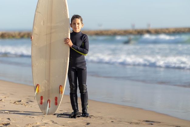 Un niño parado en la orilla del mar con una gran tabla de surf