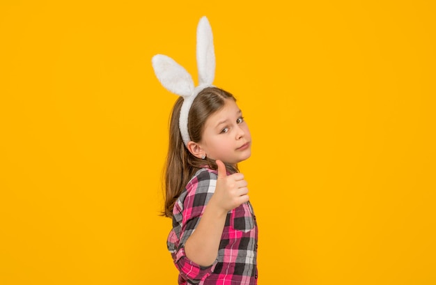 Niño de Pascua en orejas de conejo sobre fondo amarillo pulgar arriba