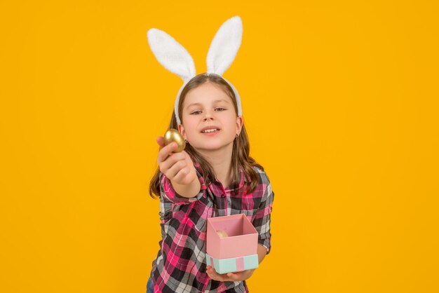 Niño de Pascua en orejas de conejo sostenga la caja y el huevo sobre fondo amarillo.