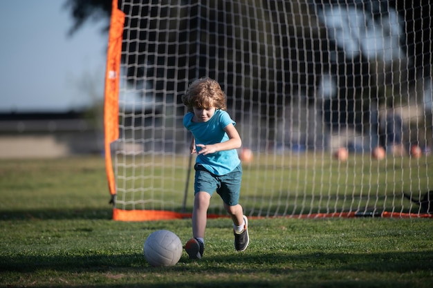 Niño pateando fútbol en el campo de deportes durante el partido de fútbol niño pateando fútbol en el campo