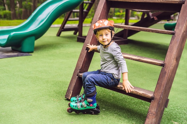 Un niño en patines en el patio de recreo El niño aprende a andar en patines el primer día y está cansado