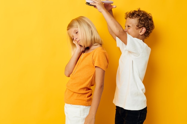 Un niño con un peine peinando el cabello de una niña con fondo amarillo.