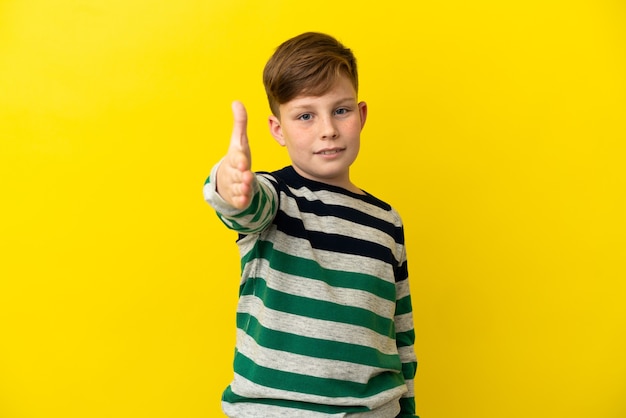 Niño pelirrojo aislado sobre fondo amarillo un apretón de manos para cerrar un buen trato