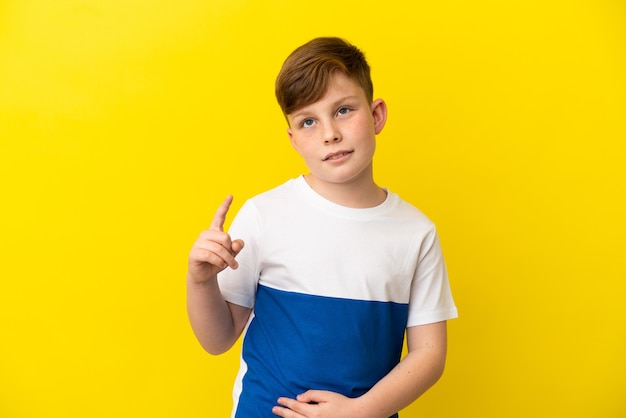 Niño pelirrojo aislado sobre fondo amarillo apuntando hacia una gran idea