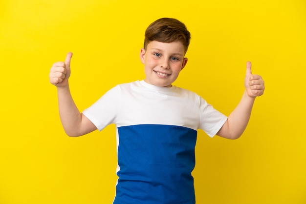 Niño pelirrojo aislado sobre fondo amarillo dando un pulgar hacia arriba gesto