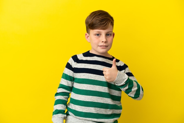 Niño pelirrojo aislado sobre fondo amarillo dando un pulgar hacia arriba gesto