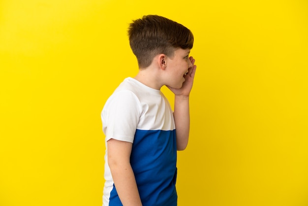 Niño pelirrojo aislado sobre fondo amarillo gritando con la boca abierta hacia un lado