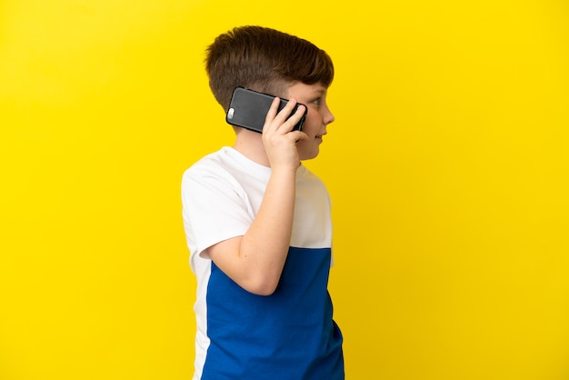 Foto niño pelirrojo aislado sobre fondo amarillo manteniendo una conversación con el teléfono móvil