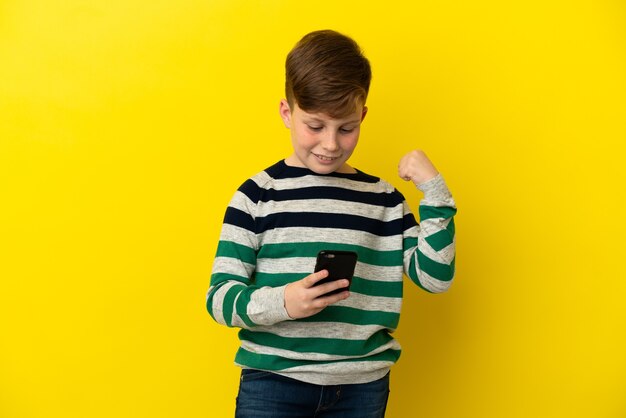 Niño pelirrojo aislado sobre fondo amarillo sorprendido y enviando un mensaje