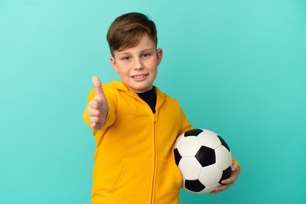 Niño pelirrojo jugando al fútbol aislado sobre fondo azul un apretón de manos para cerrar un buen trato