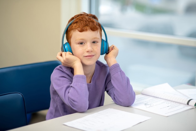 Foto niño pelirrojo sentado en el escritorio con auriculares grandes