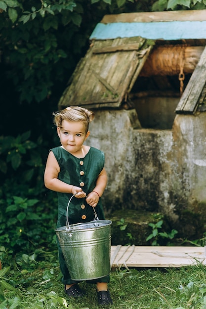 Un niño con el pelo blanco en una combinación verde juega con un cubo en la hierba