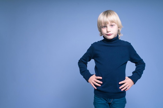 Un niño con el pelo largo y rubio tiene las manos en la cintura en el estudio