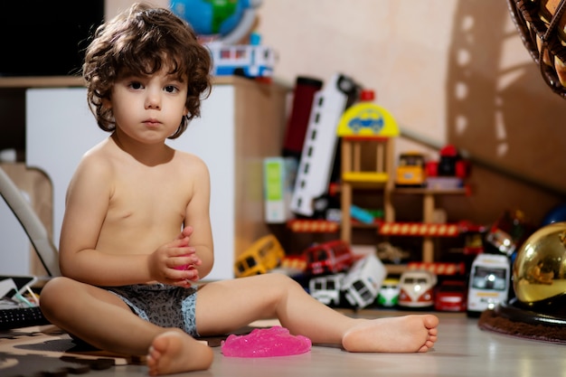 El niño de pelo rizado en pantalones cortos juega con limo en su habitación, para no ensuciarse la ropa.