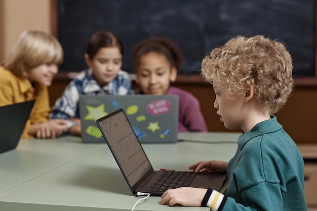 Un niño de pelo rizado usando una computadora portátil en la escuela durante la clase de informática para niños