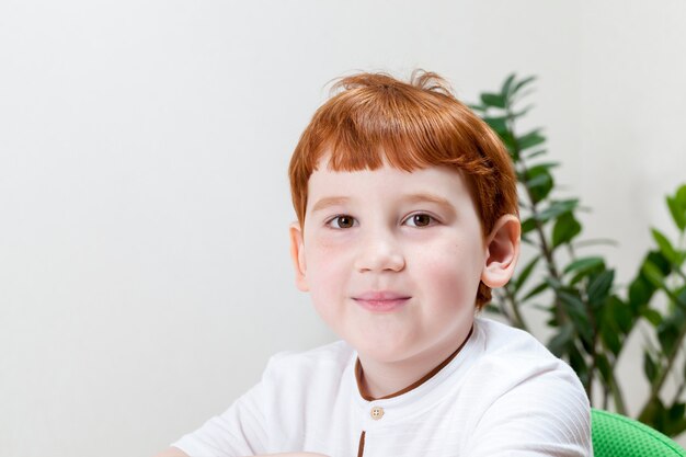 Un niño con el pelo rojo mientras estudia o trabaja, un niño dibuja con lápices de colores en una hoja de papel