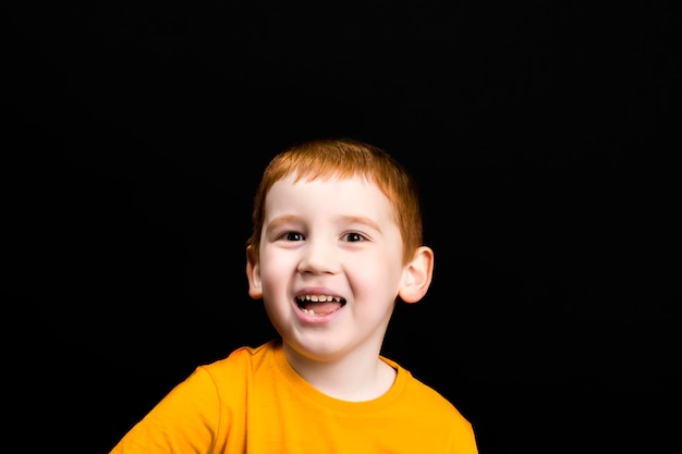 un niño con el pelo rojo sonríe y se ríe, un retrato de un niño con una cara hermosa