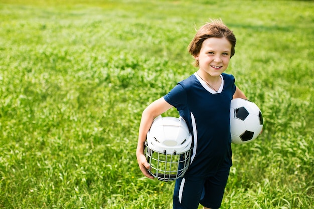 Niño con una pelota de fútbol y un casco de hockey.