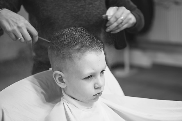 Niño en la peluquería. El niño tiene miedo de los cortes de pelo. Manos de peluquero haciendo peinado a niño, de cerca. Corte de pelo de moda para niños.