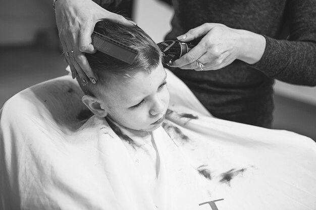 Niño en la peluquería. El niño tiene miedo de los cortes de pelo. Manos de peluquero haciendo peinado a niño, de cerca. Corte de pelo de moda para niños.