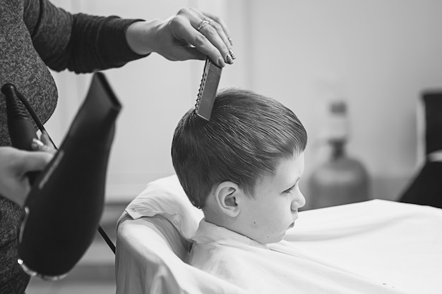 Niño en la peluquería. El niño tiene miedo de los cortes de pelo. Manos de peluquero haciendo peinado a niño, cerrar