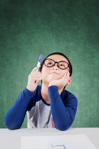 Foto niño pensativo estudiando en el escritorio contra la pared