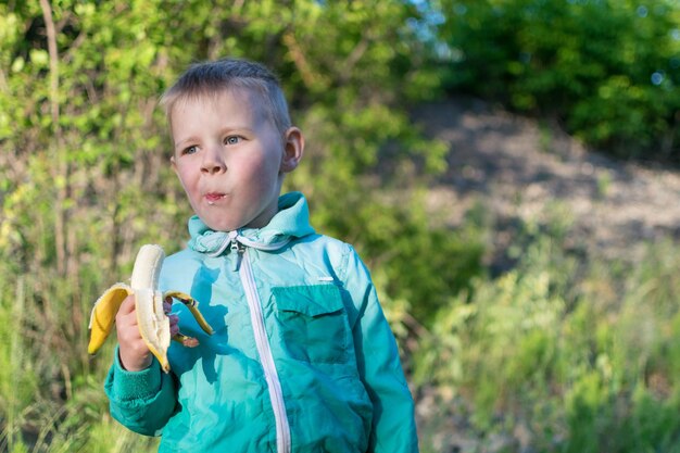 Un niño pequeño de 35 años está comiendo un plátano en la naturaleza Merienda durante un paseo al aire libre