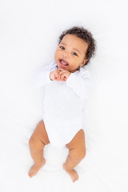 Niño pequeño afroamericano en una cama blanca en el dormitorio