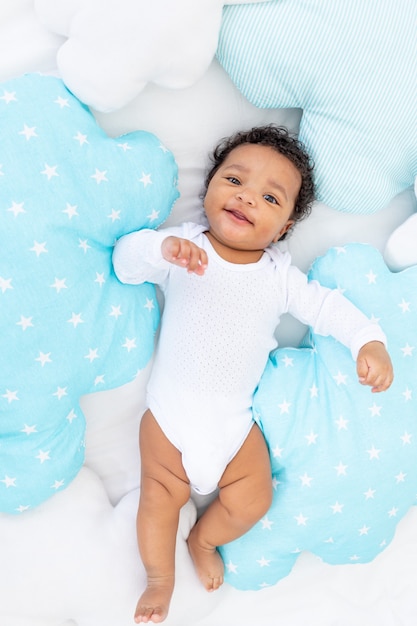Niño pequeño afroamericano sonriente en una cama blanca en el dormitorio yace en pijama