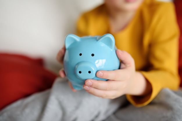 Un niño pequeño agita una hucha y sueña con lo que puede comprar.