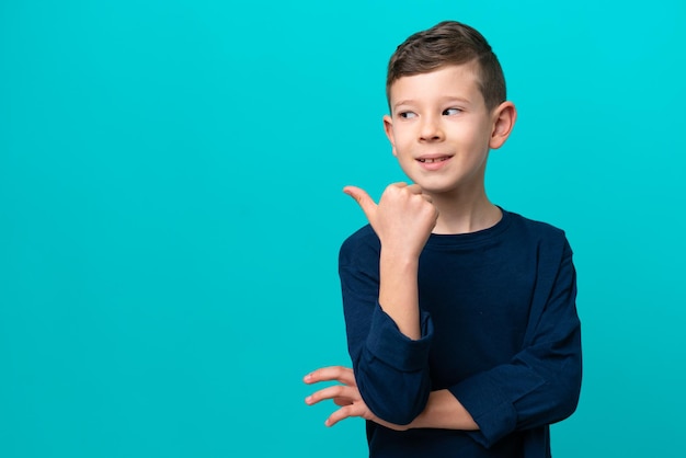 Niño pequeño aislado de fondo azul apuntando hacia un lado para presentar un producto