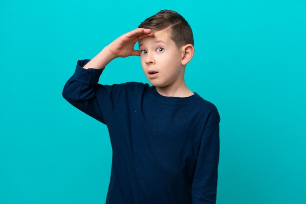 Foto niño pequeño aislado de fondo azul haciendo un gesto sorpresa mientras mira hacia un lado