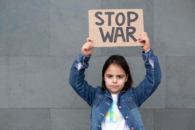 Niño pequeño aislado en una pared que muestra un cartel hecho a mano con el mensaje Stop War