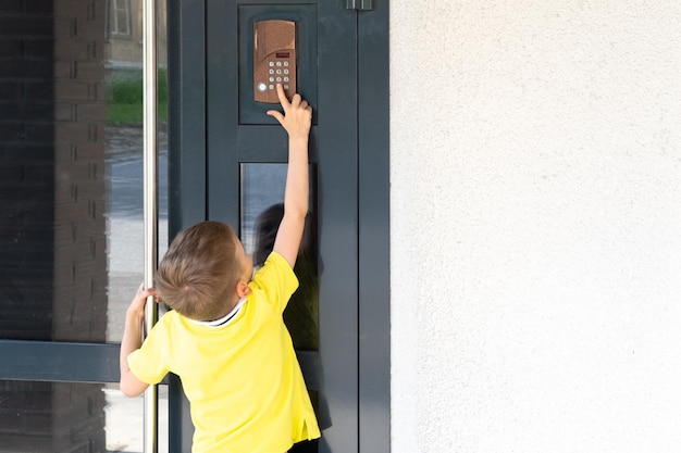 Un niño pequeño alcanza el timbre para tocar el timbre de la puerta una vista desde el espacio de la copia trasera Un niño parado cerca de la puerta principal de la casa El niño regresa a casa