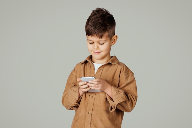 Foto un niño pequeño de años caucásicos sonrientes jugando en un juego de teléfono aislado en un estudio gris