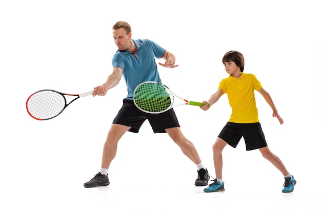 Niño pequeño aprendiendo a jugar tenis con instructor deportivo profesional aislado sobre fondo blanco de estudio