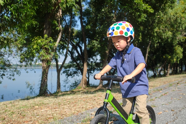 Niño pequeño asiático que usa el casco de seguridad aprendiendo a montar la bicicleta del primer equilibrio