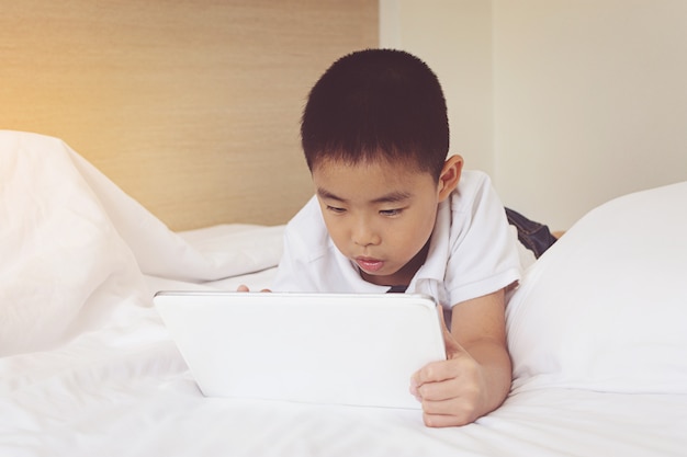 Niño pequeño asiático que usa la tableta en cama