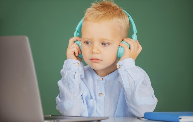 Un niño pequeño con auriculares ve una lección en video en la computadora en la escuela. El niño con auriculares tiene menos en línea.