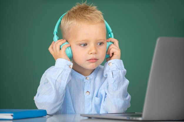 Un niño pequeño con auriculares ve una lección en video en la computadora en la escuela. El niño con auriculares tiene menos en línea.